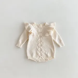 Detailed view of cream baby knit romper featuring delicate shoulder ruffles and geometric pattern.
