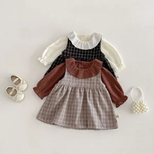 Dettaglio outfit bambina, camicetta con colletto volant e vestito scamiciato a quadri.
