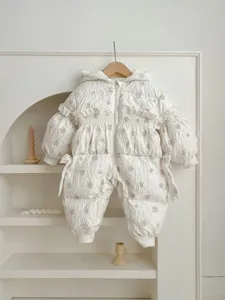 Detailed view of a cozy white baby winter down jumpsuit with cute ruffles and hood.