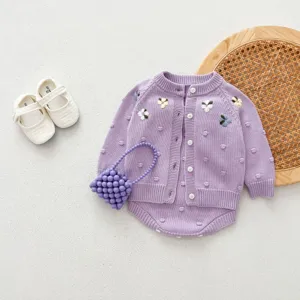 Closeup detail of baby girl purple knitted cardigan and romper with floral embroidery.
