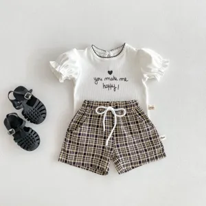 Détail d'ensemble de vêtements d'été pour bébé, haut blanc bouffant et short à carreaux.
