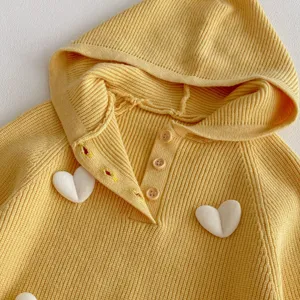 Close up of yellow knit baby hoodie sweater with cute white 3D heart details and button closure.