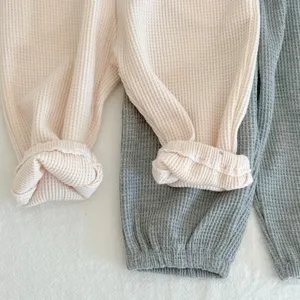Waffle knit baby pants detail close-up, soft cotton fabric, ribbed cuffs, cozy texture.