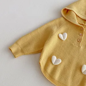 Detailed shot of cute yellow knitted hooded sweater for girls with sweet 3d white heart decor.