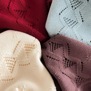 Detailed view of soft baby knitwear sweaters showing fine hollow-out patterns in vibrant colors.