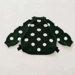 Detailed view of dark green knit baby sweater with white polka dots and cute side bows.