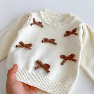 Dettaglio maglione in maglia da bambina con collo rotondo bianco e fiocchi marroni.