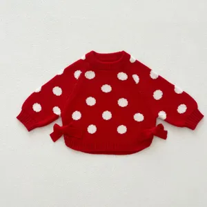 Close-up view of red knit baby sweater with white polka dots and side bows detail.