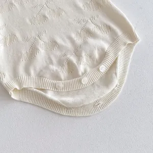 Fine knit baby romper detail, soft off-white cotton fabric, cute woven pattern and snap buttons.