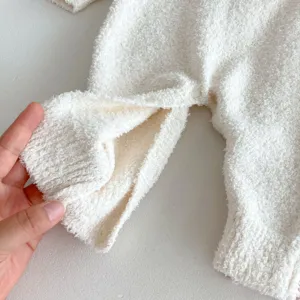 Close-up detail of white fluffy baby romper cuff and snap buttons for warm infant winter wear.