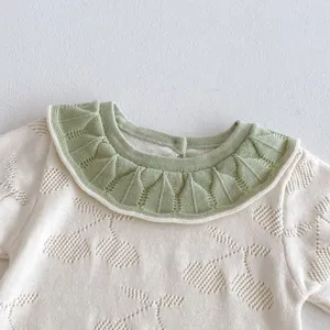 Close-up detail of infant baby knit romper with green doll collar and hollow knit pattern.