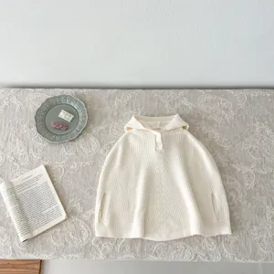 Detalle de capa con capucha de punto para bebé, suave textura de poncho lana y botón.