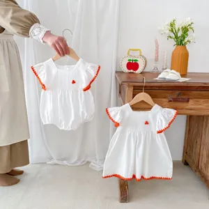 Detailed view of white baby romper and dress with orange trim, cute summer infant clothing scene.