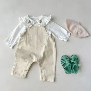 Cute baby girl autumn outfit set with white ruffle shirt and beige corduroy overalls.