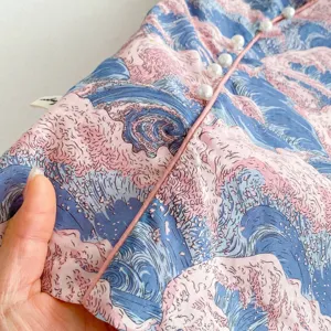Close-up detail of girls qipao dress fabric, pink blue wave pattern with pearl buttons.