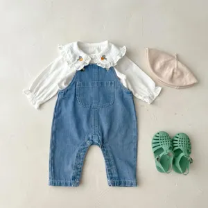 Detail shot of infant baby girl denim overalls and white blouse set with cute accessories.