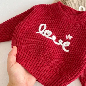 Red knit sweater detail for young girls, cute embroidered love pattern, cozy long sleeve top.