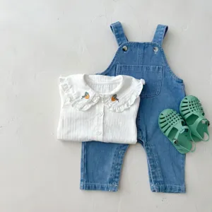 Baby clothing set detail view featuring white ruffled blouse, denim overalls and jelly sandals.