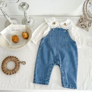 Detailed shot of infant baby girl cotton denim overalls and cute ruffled collar white blouse.
