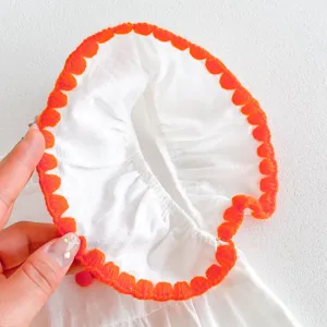 Close-up detail shot of baby dress white fabric with vibrant orange crochet lace trim.