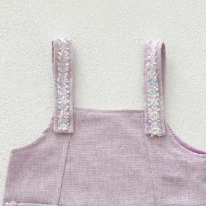 Charmant détail de robe en tweed violet pour fille, avec bretelles tressées colorées.