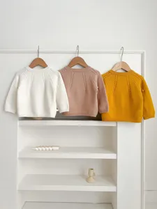 Infant knit sweater detail, solid color round neck cardigan hanging on white shelf aesthetic background.