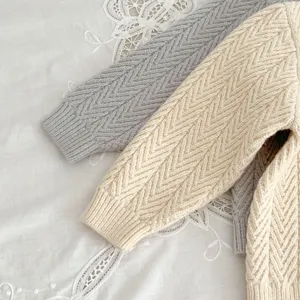 Primer plano detallado de cómodos jerséis de punto para bebé con patrón de espiga en beige y gris.