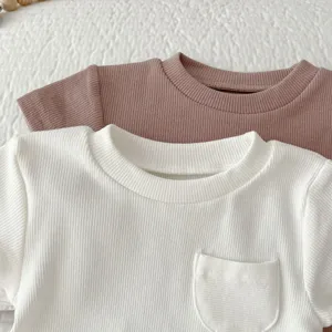 Detailed close-up of ribbed cotton baby t-shirts in white and mauve, soft collar, pocket.