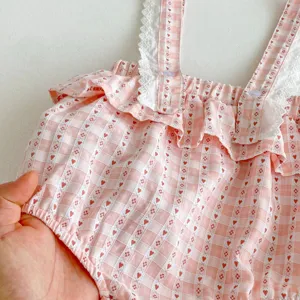 Primo piano dettagliato della tutina per neonata rosa a quadretti con cuori e pizzo bianco.