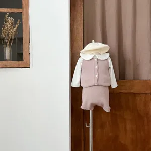 Vue détaillée de l'ensemble tricot pour bébé, avec gilet rose, chemisier blanc et joli bonnet.