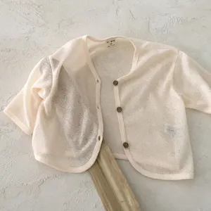Detail shot of cream baby cardigan, lightweight sheer knit texture, wooden buttons, infant top.