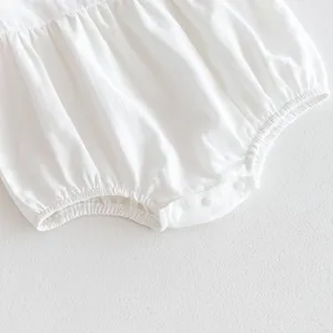 Detailed close-up shot of a white newborn baby romper featuring soft ruffles and snap buttons.