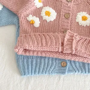 Close-up detail of cute baby knit cardigan with sweet daisy embroidery and wooden buttons.