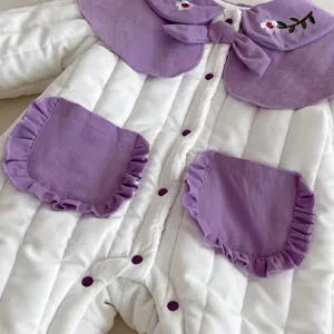 Close up of baby winter padded jumpsuit detail, white quilted fabric with purple ruffles.