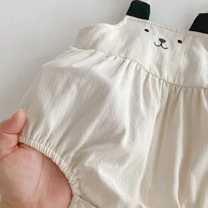 Λεπτομέρεια βρεφικού cotton romper με κεντημένο προσωπάκι αρκούδας και μαύρα τιραντάκια.