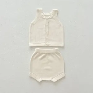 Vue rapprochée détaillée de l'ensemble tricoté bébé crème, gilet et short bouffant.