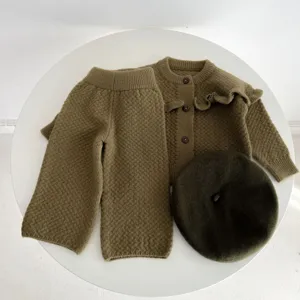 Dettaglio del set in maglia per neonati con cardigan con volant, pantaloni e berretto abbinato.