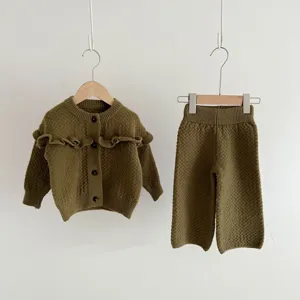 Vista dettagliata del set cardigan e pantaloni in maglia verde oliva con bottoni in legno.