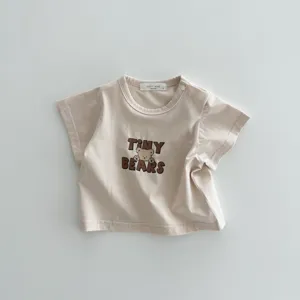 Dettaglio t-shirt neonato in cotone a maniche corte con stampa orsetto e etichetta.