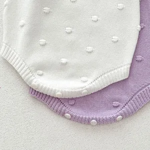Infant knitted baby romper detail close-up showing soft cotton texture and cute bobble dots.