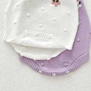 Infant knit baby romper detail close-up, soft cotton yarn texture with delicate hand embroidery.