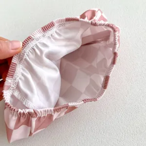 Vue détaillée de maillot de bain pour bébé en tissu à carreaux roses et blancs élastique.