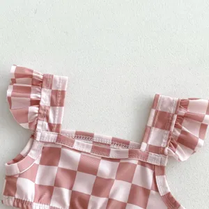 Gros plan sur les détails du maillot rose à carreaux pour bébé, avec bretelles à volants.