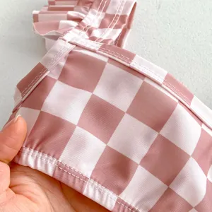 Détail du tissu de maillot de bain bébé à carreaux rose et blanc, texture douce et volants.