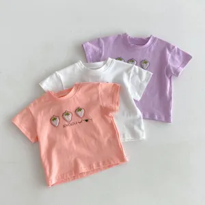 Λεπτομέρεια από βαμβακερά παιδικά t-shirts με γλυκό κέντημα φράουλας σε τρία παστέλ χρώματα.