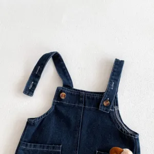 Détail de salopette en denim pour bébé avec tissu bleu foncé, boutons et jolie poche.
