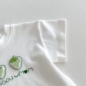 Λεπτομέρεια λευκό βρεφικό t-shirt, χαριτωμένο πράσινο κέντημα φράουλας, μαλακό βαμβακερό καλοκαίρι.