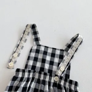 Black and white plaid baby romper detail featuring delicate lace strap trim and cute white buttons.