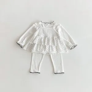 Detailed view of baby girl three-piece outfit, white ruffled tee, polka dot camisole, leggings.