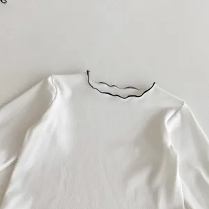Detailed view of the white ribbed long sleeve top featuring a stylish black lettuce edge collar.